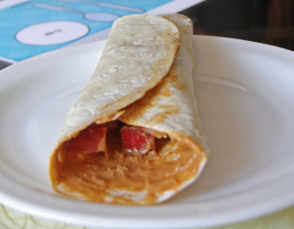 A rolled tortilla filled with apples and peanut butter on a plate.