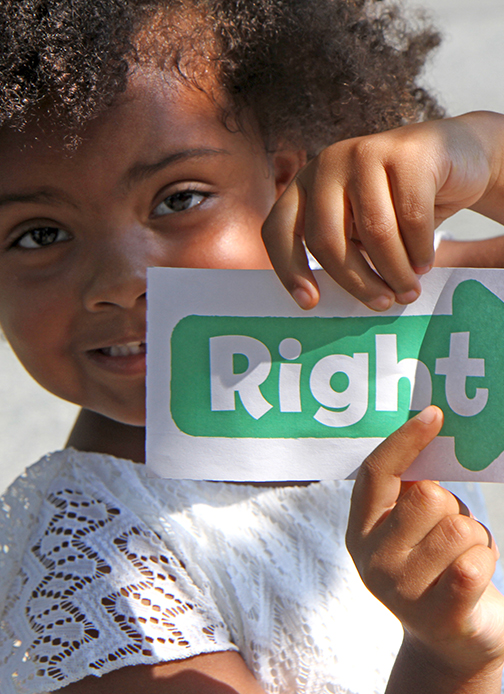A young girl holds up a paper arrow with the word “Right” written on it.