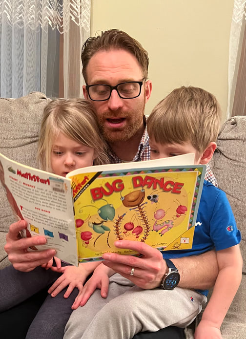 A father reads the book “Bug Dance” by Stuart J. Murphy to two children.