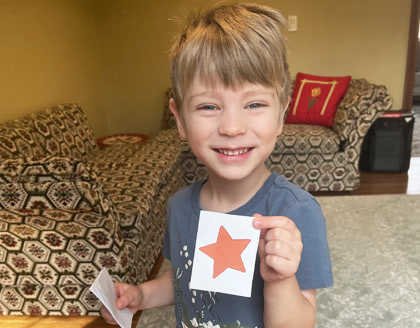 A young boy holds up a printed out star and smiles.