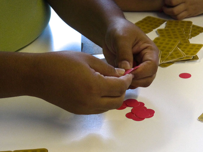 Close-up of a child’s hands holding some paper berries while other berries and paper waffles sit in piles on the table.