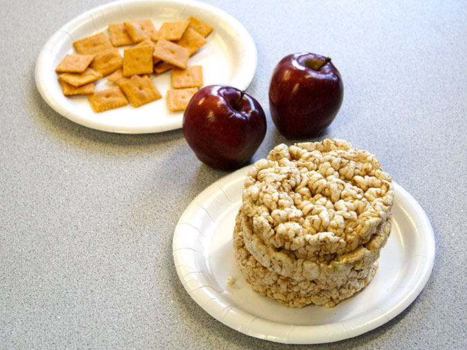 Close-up of a plate of crackers, a plate of rice cakes, and two apples.
