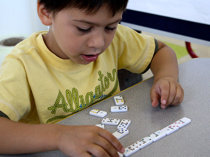 A boy matches adds a domino to a line he has made with dominoes that match end to end.