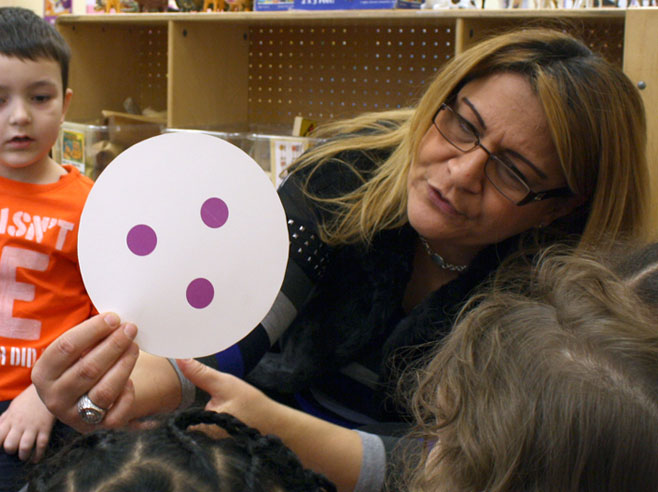 A teacher holds up a Dot Plate with three purple dots while a group of children watch.