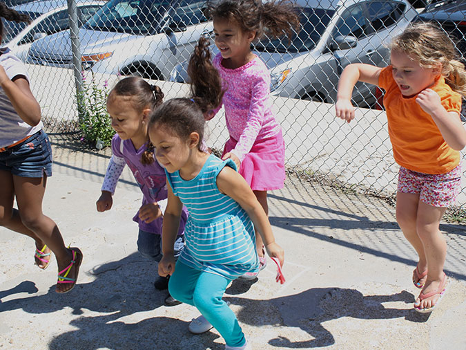 Children hop away from a fence bordering the playground pavement.