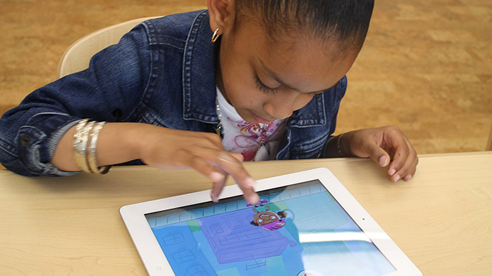 A preschool girl wearing a jean jacket plays the Early Math with Gracie & Friends City Skate app by tapping the screen to make the character in the app jump.