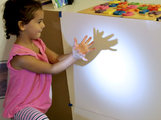 A student kneels and creates shadow patterns with her hands against a spot lit wall.