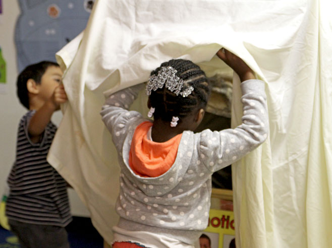 Two students work to set up a shadow theatre. They are draping a large white sheet over a classroom puppet stage.