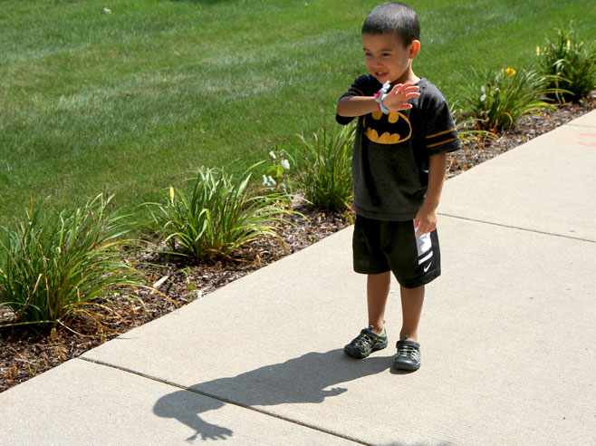 A student stands on a sidewalk and waves at his shadow.