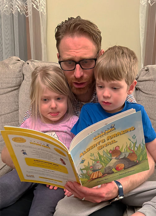 A father reads the book “Albert’s Amazing Snail” by Eleanor May to two children.