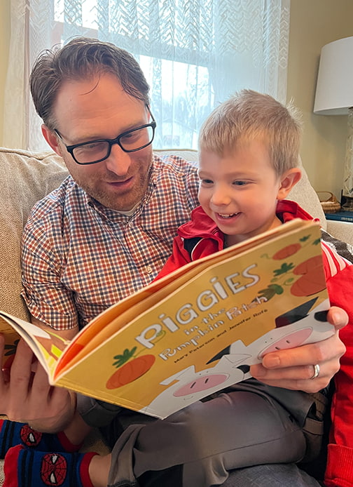 A father and his child read the book “Piggies in the Pumpkin Patch” by Mary Peterson and Jennifer Rofé.