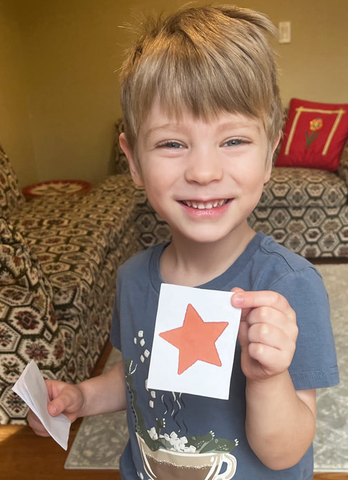A young boy holds up a printed out star and smiles.