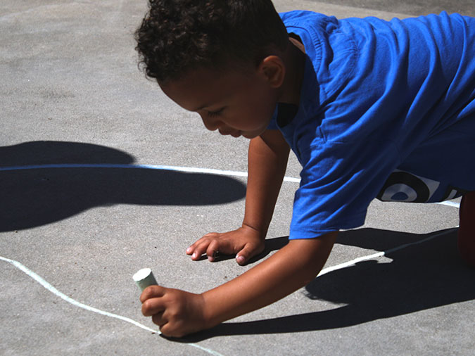 A boy in a blue shirt uses chalk to divide the hopscotch circle into equal slices.