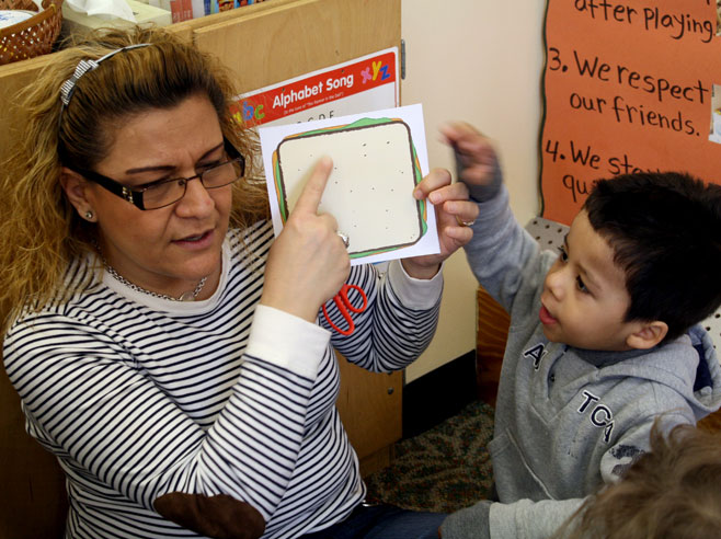 A teacher points to a paper sandwich while a boy looks on and points to it.