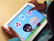 A young girl holds an iPad showing the Gracie and Friends Park Play app on-screen.