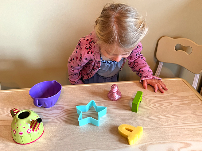 A girl looks at a table at differently-shaped objects from above.