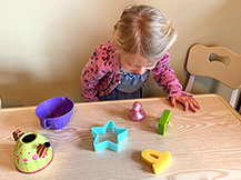 A girl looks at a table at differently-shaped objects from above.