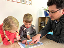 A man points to a map of the United States of America on a table with a boy and a girl.