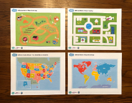 Four different map printouts, depicting a farm, a city, the United States, and the world, laid out on a table.