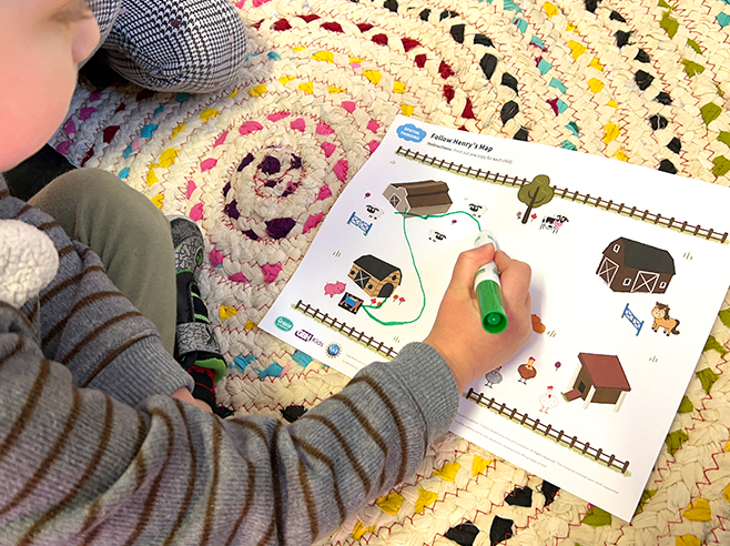 A boy draws a pathway between landmarks on a farm scene.