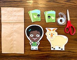 A paper bag next to scissors, tape, and printouts of the Gracie character, a goat, and spatial vocabulary cards.