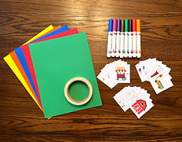 A stack of brightly colored paper next to tape, markers, and printouts of farm, fair, and city landmarks.