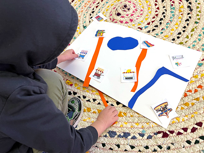 A boy places paper strips and landmarks on a piece of paper to make a map.