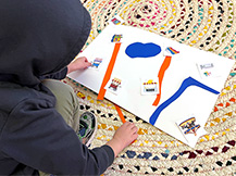 A boy places paper strips and landmarks on a piece of paper to make a map.