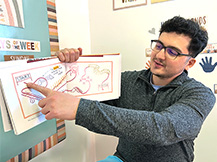 A man points to a pathway around landmarks in Julie Dillemuth’s book “Mapping My Day” as he holds up the book.