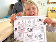 A smiling girl holds up a printout of a maze with a pathway hand drawn from the start to finish.