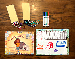 Julie Dillemuth’s book “Mapping My Day” next to a hand-drawn map on a clipboard, a pile of markers, and small treasure boxes.