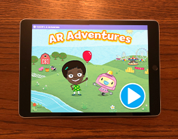 An iPad screen of the “AR Adventures” augmented reality app showing the character Gracie holding a balloon and standing next to a robot.