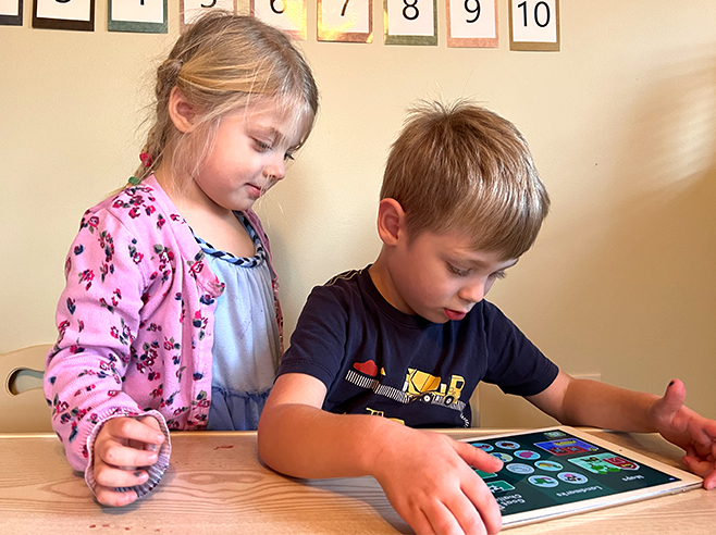 A boy plays the Gracie & Friends “Map Adventures” preschool spatial thinking app while a girl watches.