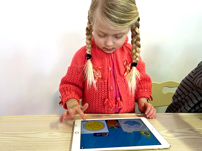 A girl swirls laundry around in digital dryer as she plays the Gracie & Friends “Map Adventures” preschool spatial thinking app.