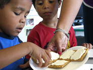 A teacher holds out a plate of snacks to two young boys.