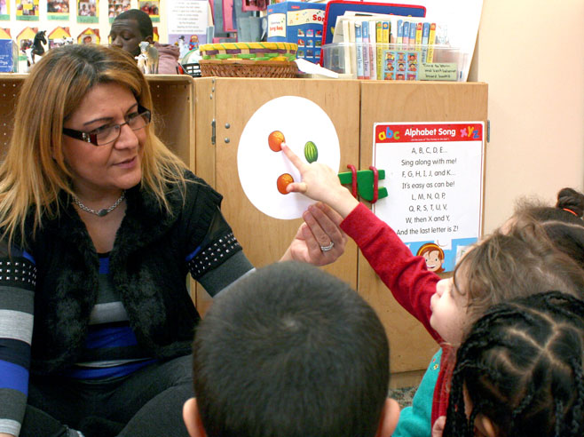 A young child points to a picture of an orange on a round card held by her teacher.