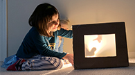 Child makes shadows in a shadow box theater.