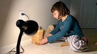 Child stacks blocks to shade a stuffed animal from lamp.