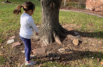 Child points to her shadow on the ground outside.