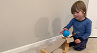 Child rolling a ball down an obstacle course.