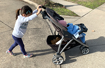 Child pushing a stroller up a driveway ramp.