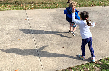 Un niño y una niña haciendo sombras mientras bailan afuera.