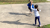 Two children making shadows while dancing outside.