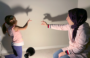Parent and child making shadows on the wall with their hands.