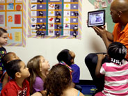 Teacher holds up iPad to show video to class.