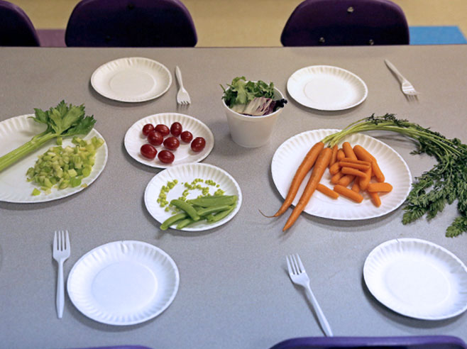 A buffet table with vegetables, plates, and forks.