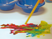 A close up of paint on paper being moved around by someone blowing through a straw.