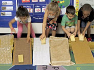 Four students slide wooden blocks down cardboard ramps covered in different textured materials.