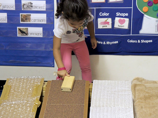 A student slides a wooden block down a cardboard ramp covered in sandpaper.