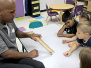 Students watch teacher slide a binder clip down a ramp made from half a cardboard tube.